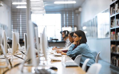 Group of young students sat in a library working on bank of computers