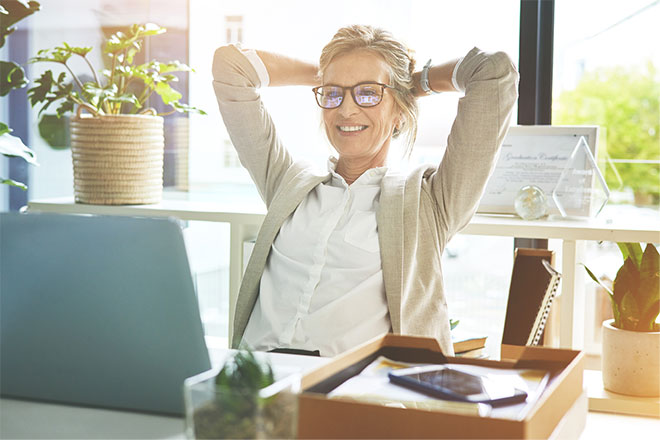 Lady leaning back in chair with hands behind head smiling at laptop screen