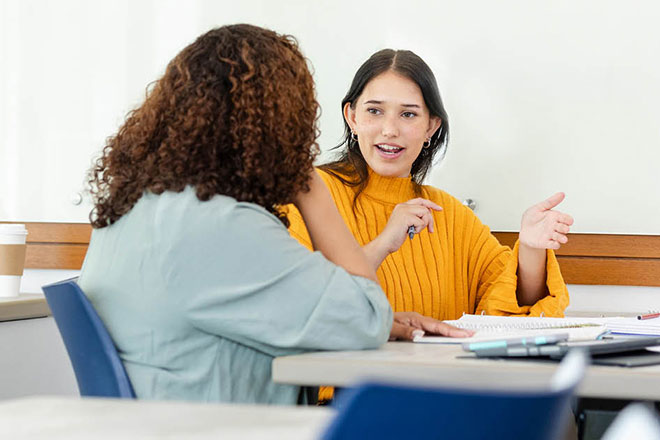 Two women sat talking to each other in a classroom